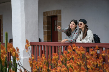 Wall Mural - two asian taiwanese women visitors admiring garden flowers with pointing gesture from the balcony of old mission santa Barbara during their spring trip in California usa