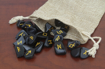 Wall Mural - Close up of black stone runes with burlap sack on wooden background.