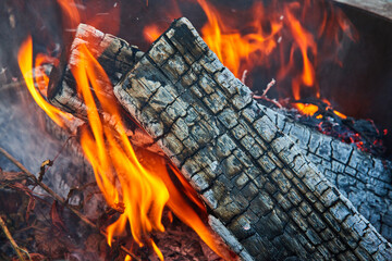 Orange and yellow flames licking at underside of two charred logs with smoke