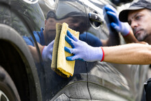 Professional car wash worker in workwear detailing and wiping car with rag outside