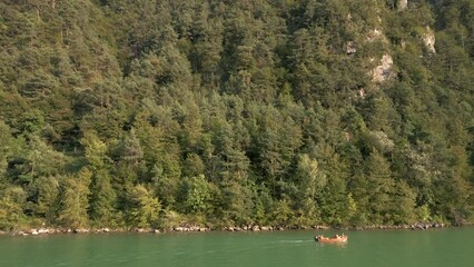 Sticker - Drone shot of small boat sailing on the sea and a mountain covered by trees behind it