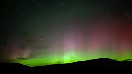 Wall Mural - bright green and red aurora flash in a star filled sky above rolling hills. the big dipper can be se
