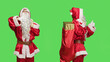 Leinwandbild Motiv Santa does thumbs up and thumbs down against greenscreen background, carrying sack of presents on camera. Undecided saint nick shows like and dislike sign, wearing famous costume.