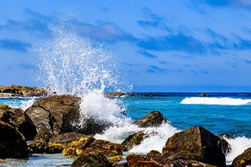 Poster - Scenic beach scene featuring a rocky shoreline with blue waters in the background