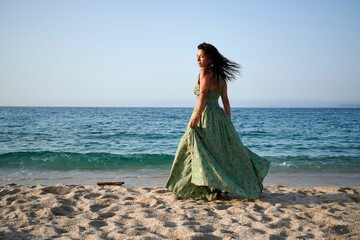 Poster - Young woman on a beach in Sardinia, Italy with the wind blowing her green dress on a sunny day