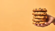 Hand holding chocolate chip cookies isolated on orange background, copyspace for text, American cookie