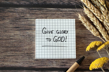 Wall Mural - Give glory to God, handwritten Christian quote with pen, ripe wheat ears and flowers on wooden table. Top view. Praise, worship, thanksgiving, and blessing LORD Jesus Christ, biblical concept.