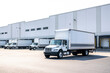 © vit - Huge warehouse building with docks and gates and loading cargo middle duty day cab rigs semi trucks with box trailer preparing for the next local deliveries