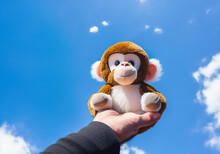 A Hand Holding A Stuffed Monkey Toy Against A Blue Sky Background, Soft Focus