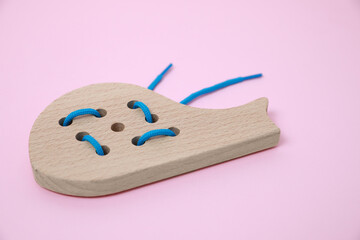 Sticker - Wooden whale figure with holes and lace on pink background. Educational toy for motor skills development