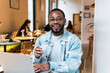 © BUDDHA - Happy african casual man in glasses sits at cafe table looking at camera, cheerful black student posing studying with book in coffee house, smiling businessman works on laptop in cafeteria, portrait