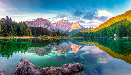 calm morning view of fusine lake. colorful summer sunrise in julian alps with mangart peak on backgr