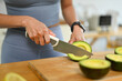Woman slicing avocado with knife on a cutting board, preparing healthy breakfast in kitchen. Healthy eating concept