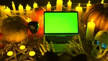 Close Up. Bony Monster Hands Typing At Laptop Keyboard With Green Screen, Creepy Post Social Media, Candles In Cobwebs, Pumpkins, Skull. Horror Atmosphere Happy Halloween. Advertising Scary Game.