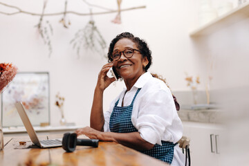 Wall Mural - Happy flower store owner talking with her clients on a phone call