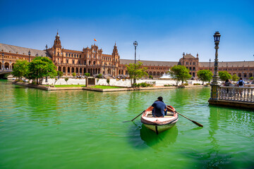 Poster - Sevilla, Spain - April 10, 2023: Several boats with people rowing at leisure on the lake of Plaza de Espana with buildings in the background