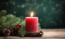 Burning red Christmas candle on the table. Christmas tree branches and pine cone on a wooden table on a green background.