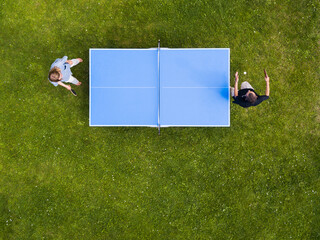 Aerial view people playing ping pong match outdoor. Top view two boys playing table tennis on a green grass lawn. Aerial view outdoor sport