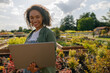 © Kostiantyn - Woman gardener working on laptop while sitting on background of shop plants center