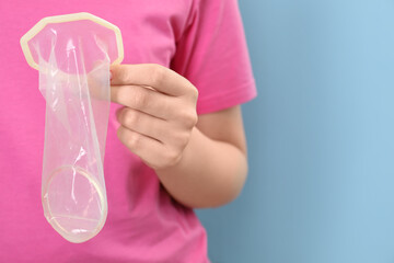 Wall Mural - Woman with unrolled female condom on light blue background, closeup. Space for text