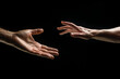 © sderbane - Two male hands reaching towards each other, dark background