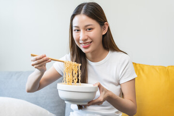 Happy temptation, cute attractive asian young student woman, girl using chopsticks eating instant ramen, noodles soup in bowl in living room at home, cooking meal fast food lifestyle of person.