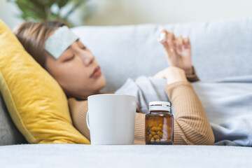 sick, influenza asian young woman put fever cooling patch on forehead, lying rest on sofa covered bo