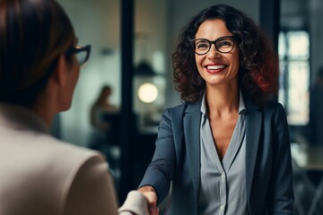 Happy mid-aged businesswoman manager shakes hands with a client in the office, sealing a successful deal. A smiling female executive makes a successful partnership agreement