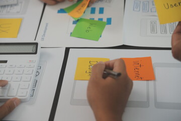 Close up ux developer and ui designer brainstorming about mobile app interface wireframe design on table with customer breif and color code at modern office.Creative digital development agency