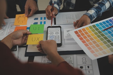 Close up ux developer and ui designer brainstorming about mobile app interface wireframe design on table with customer breif and color code at modern office.Creative digital development agency