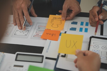 Close up ux developer and ui designer brainstorming about mobile app interface wireframe design on table with customer breif and color code at modern office.Creative digital development agency