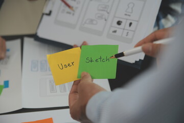 Close up ux developer and ui designer brainstorming about mobile app interface wireframe design on table with customer breif and color code at modern office.Creative digital development agency