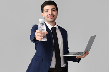 Canvas Print - Young businessman with bottle of water and laptop on grey background