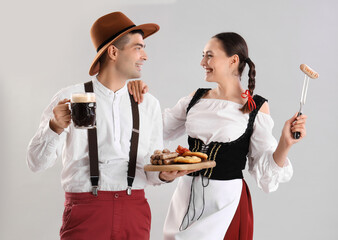 Young couple in traditional German clothes with beer and snacks on light background