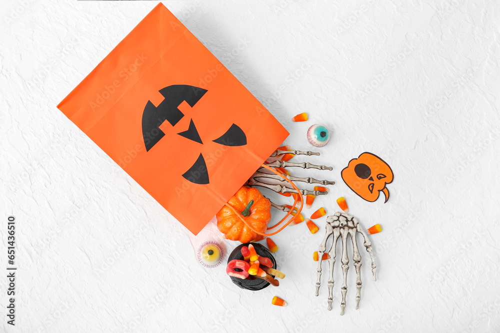 Composition with shopping bag, skeleton hands and tasty candy corns for Halloween on light background