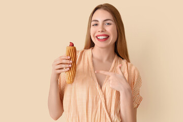 Canvas Print - Pretty young woman pointing at tasty french hot dog on beige background