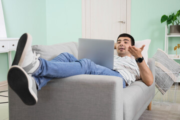 Canvas Print - Young man with laptop video chatting on sofa at home