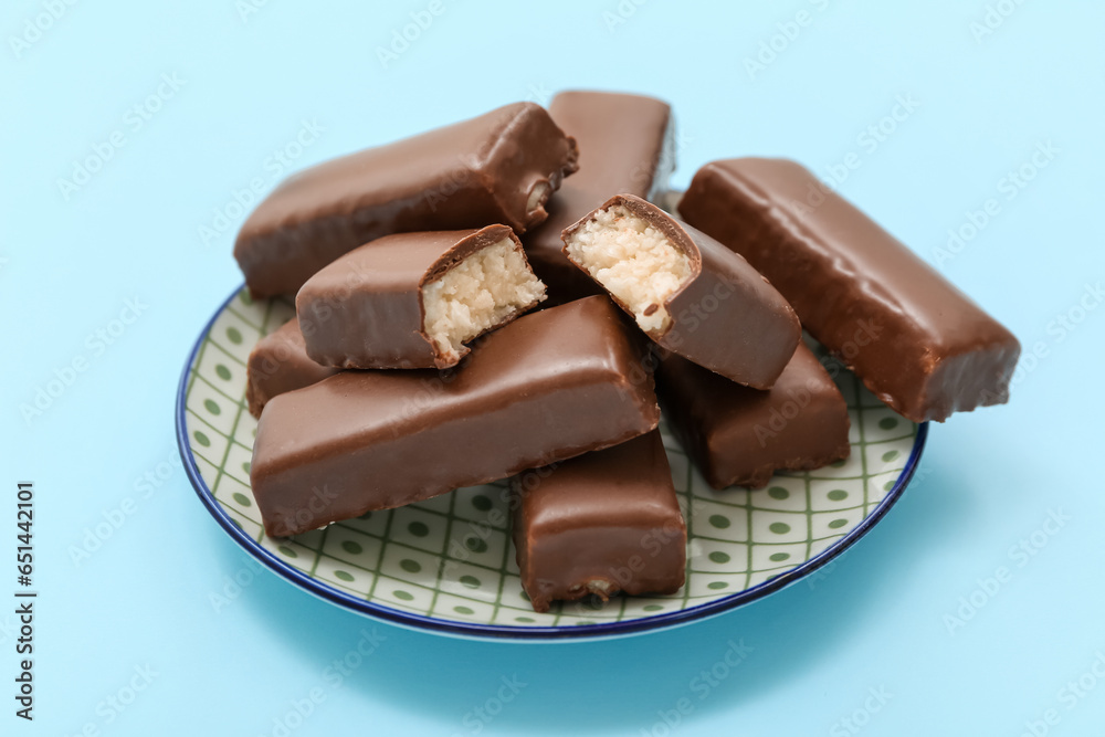 Plate with tasty chocolate covered coconut candies on blue background
