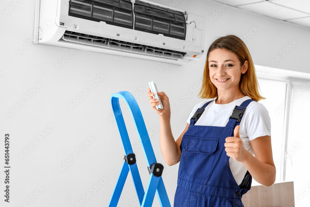 Female technician with air conditioner showing thumb-up in room