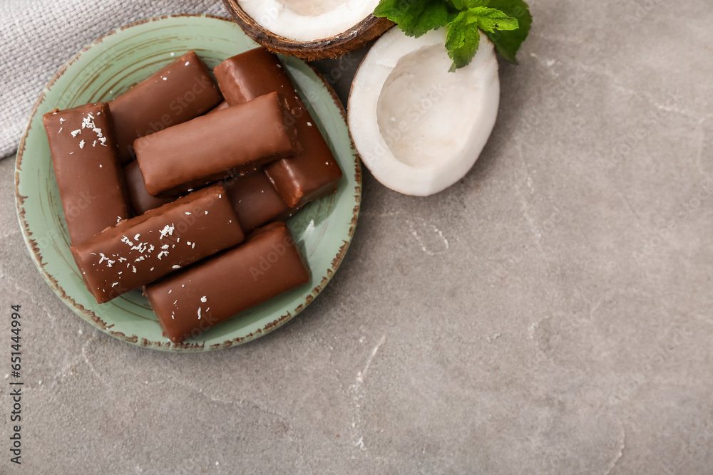 Plate with tasty chocolate covered coconut candies on grey background