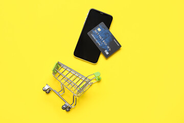 Wall Mural - Shopping cart with mobile phone and credit card on yellow background