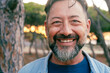 © simona - Close up portrait looking on camera of adult mature man with beard and big smile at the park. Aged male person in cheerful expression. One male 50s enjoy leisure activity outside in nature outdoors