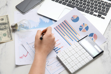 Poster - Female hand with charts, calculator, laptop and light bulb on white marble table. House rent concept