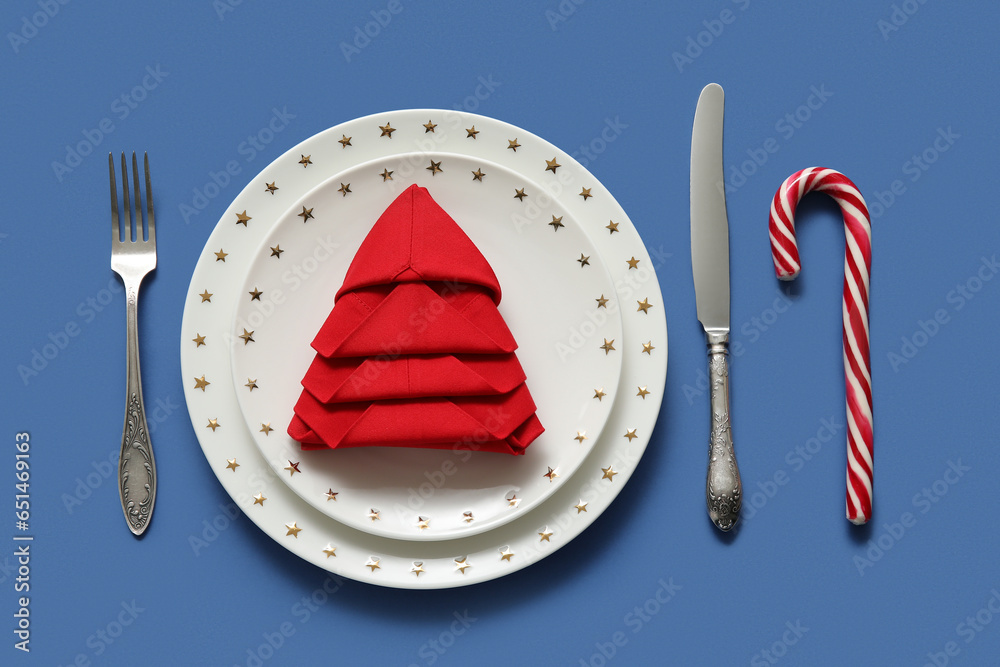 Festive table setting with folded napkin and Christmas decorations on blue background, closeup