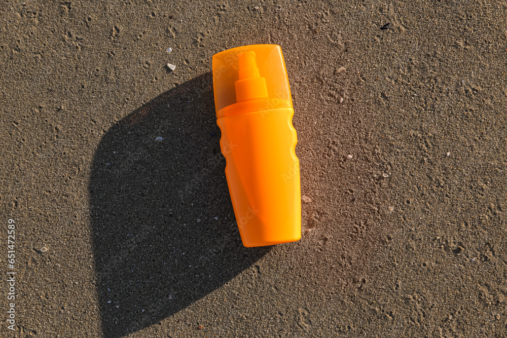 Bottle of sunscreen cream on sand at sea beach