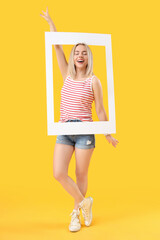 Poster - Young beautiful happy woman with frame on yellow background