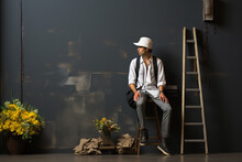 Minimalistic Plot, A Young Man In A Hat Sitting On A High Chair. Copy Space.