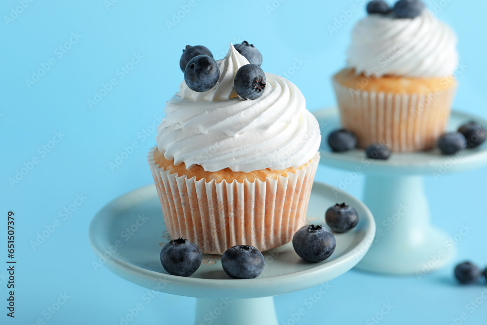 Stand of tasty cupcake with blueberries on blue background