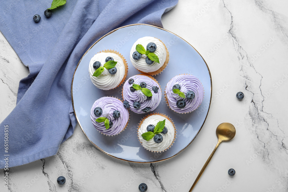 Plate of delicious cupcakes with blueberries and mint on white background