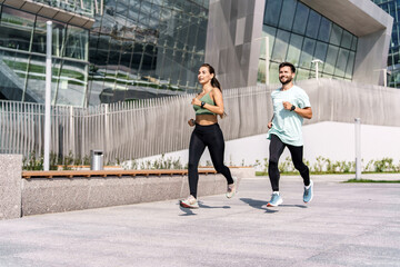 Friends running athletes in fitness clothes training outdoors. Man and woman warm up for cardio fitness. Young people lead an active and healthy lifestyle.